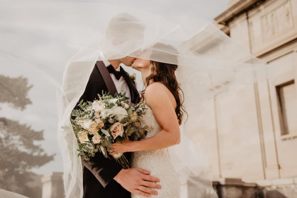 A bride and groom share a kiss behind the sheer veil of the bride