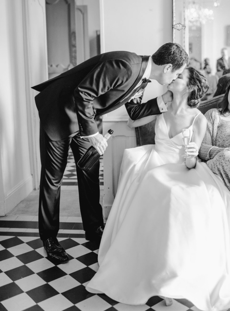 the groom leans over and kisses the bride sitting on the chair